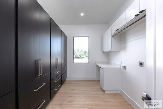 washroom featuring light wood-style floors, hookup for an electric dryer, cabinet space, and baseboards