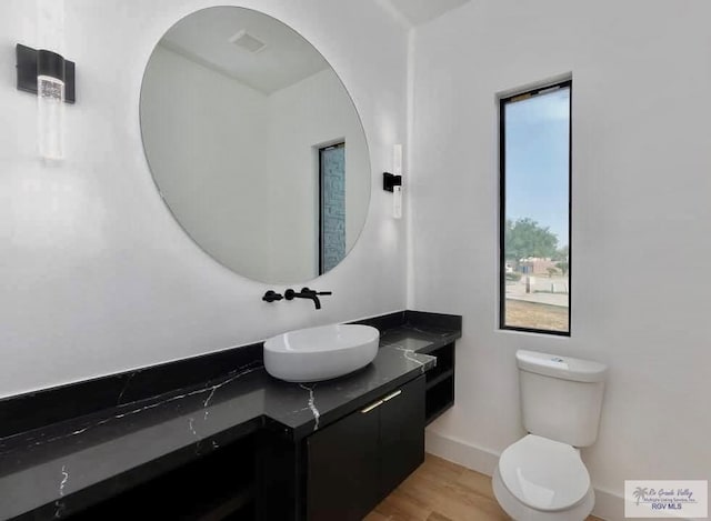 half bathroom featuring toilet, baseboards, wood finished floors, and vanity