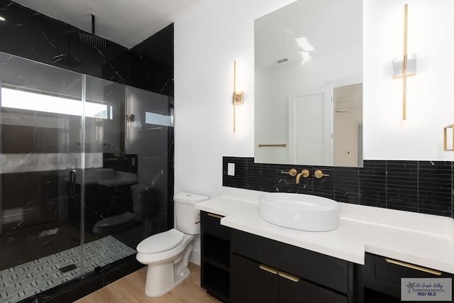 bathroom with toilet, wood finished floors, vanity, a shower stall, and decorative backsplash