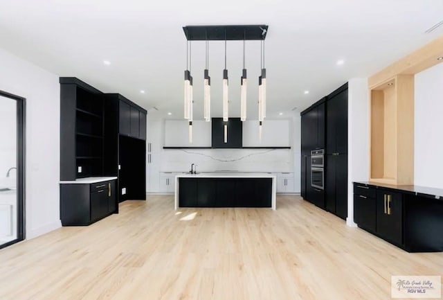 kitchen featuring light wood-style floors, backsplash, dark cabinets, and a center island