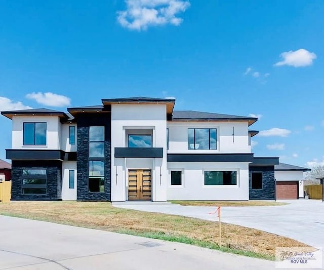 view of front of property featuring concrete driveway, stone siding, stucco siding, an attached garage, and a front yard