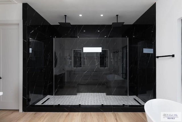 full bathroom with wood finished floors, a soaking tub, and a marble finish shower