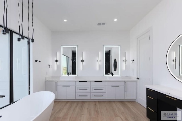 full bath featuring vanity, wood finished floors, a freestanding tub, and visible vents