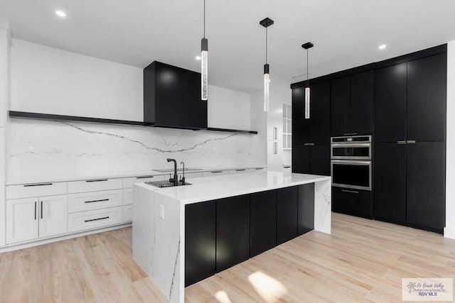 kitchen with double oven, dark cabinetry, light wood finished floors, and white cabinetry