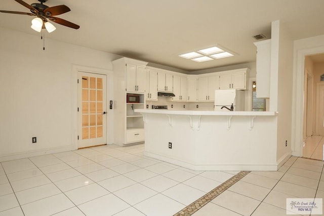 212 E Xenops Ave, Mcallen, TX 78504 - kitchen with freestanding refrigerator, light countertops, under cabinet range hood, a peninsula, and a kitchen bar