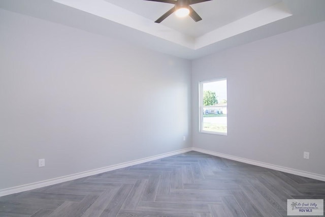 unfurnished room with ceiling fan, a raised ceiling, and dark parquet floors