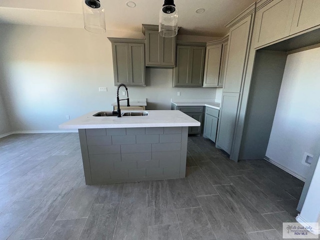 kitchen featuring pendant lighting, sink, gray cabinetry, and a kitchen island with sink