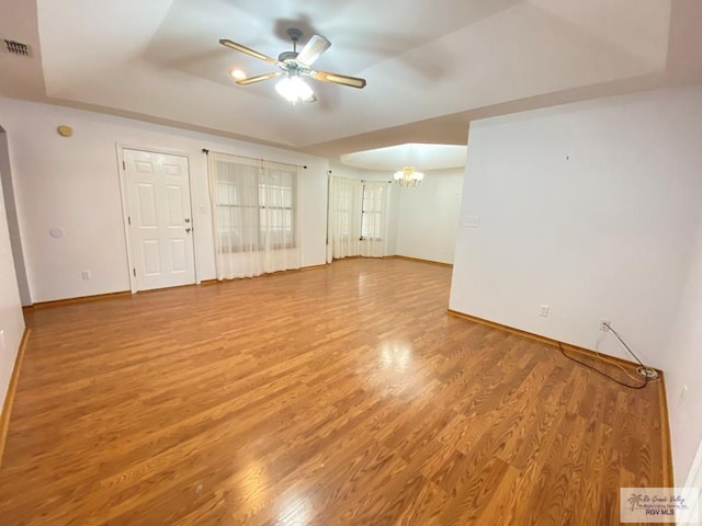 empty room with ceiling fan with notable chandelier, wood-type flooring, and a raised ceiling