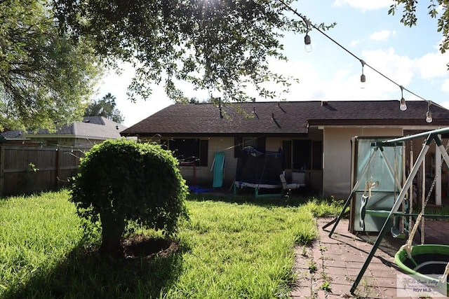 rear view of house with a playground, a yard, and a trampoline