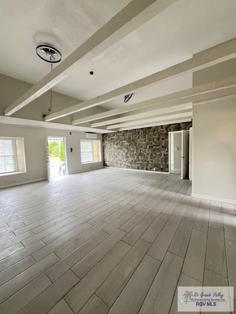 unfurnished living room with beamed ceiling, wood tiled floor, and a healthy amount of sunlight