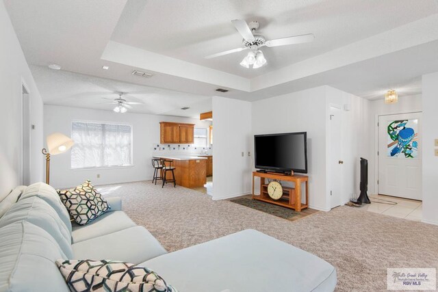 carpeted living room with a raised ceiling and ceiling fan