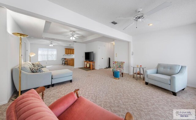 living room with a raised ceiling, light carpet, and ceiling fan