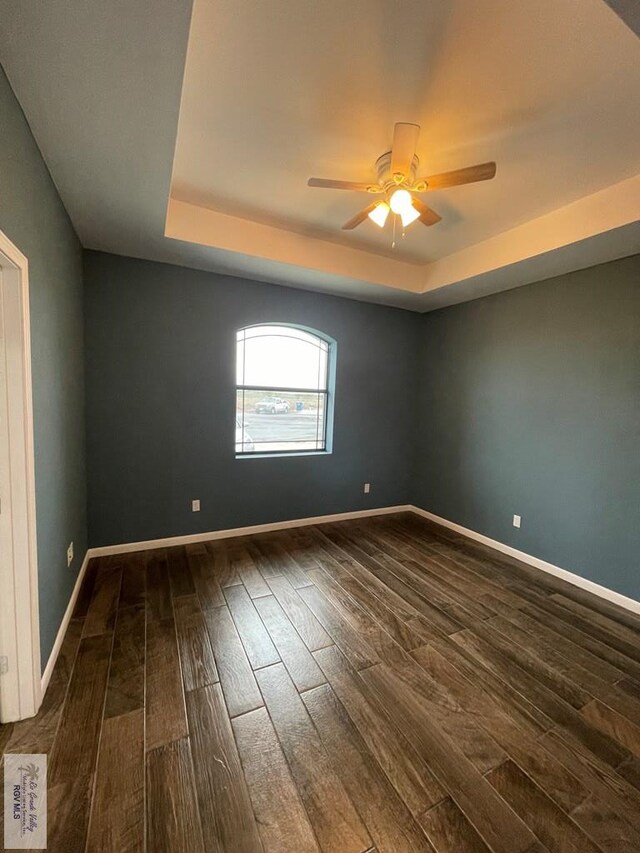 spare room featuring dark hardwood / wood-style flooring, ceiling fan, and a raised ceiling