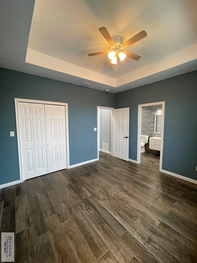 unfurnished bedroom featuring a raised ceiling, ceiling fan, dark wood-type flooring, and two closets