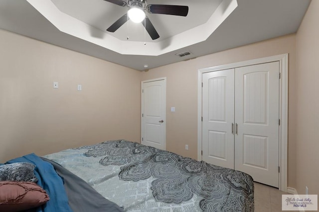 bedroom with a closet, light tile patterned floors, a raised ceiling, and ceiling fan