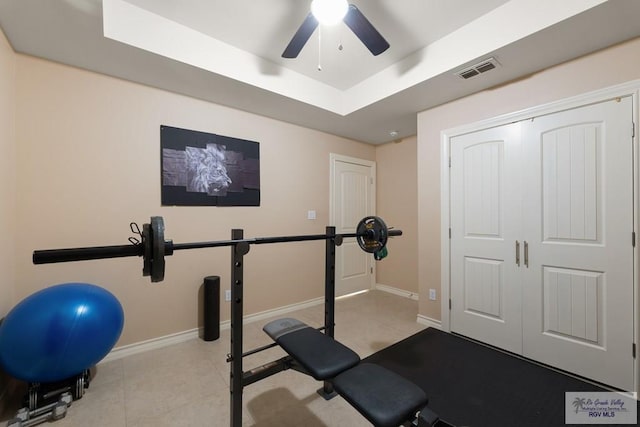 exercise room with a raised ceiling, light tile patterned floors, and ceiling fan