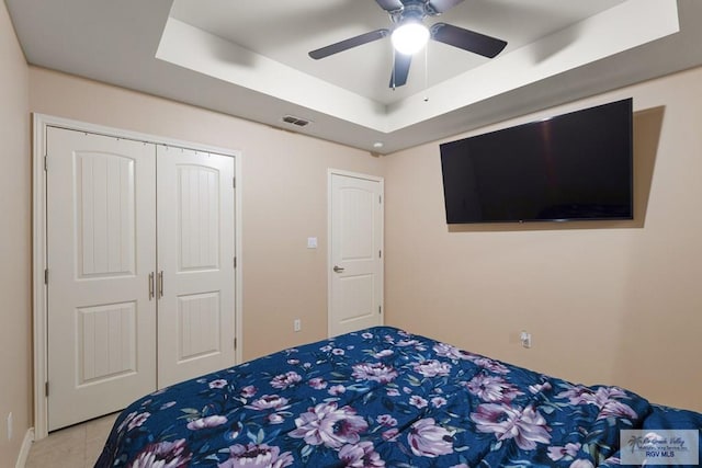 bedroom featuring a raised ceiling, light tile patterned floors, ceiling fan, and a closet