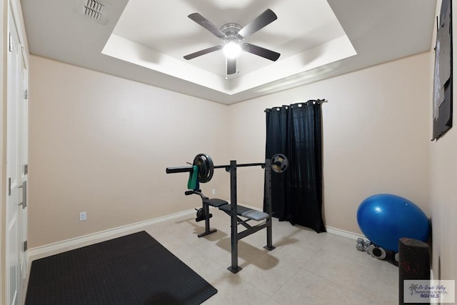 workout room featuring light tile patterned floors, a tray ceiling, and ceiling fan