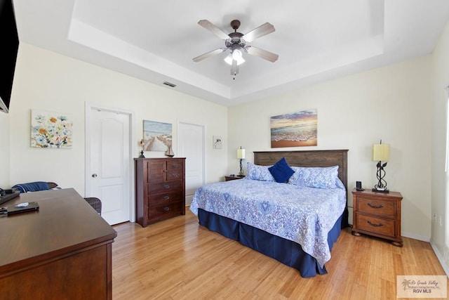 bedroom with ceiling fan, visible vents, baseboards, light wood-style floors, and a tray ceiling