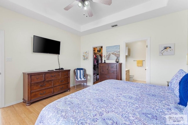 bedroom with visible vents, baseboards, a walk in closet, light wood finished floors, and a raised ceiling