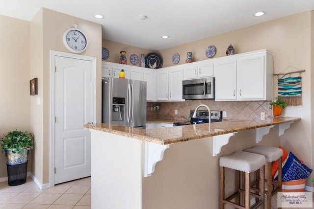 kitchen featuring decorative backsplash, a peninsula, stainless steel appliances, white cabinetry, and light tile patterned flooring