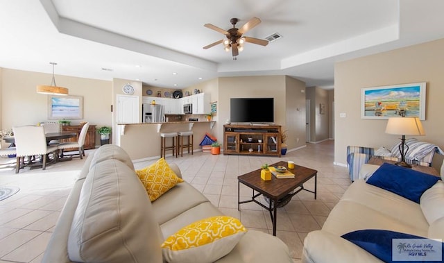 living area with light tile patterned floors, a raised ceiling, visible vents, and a ceiling fan