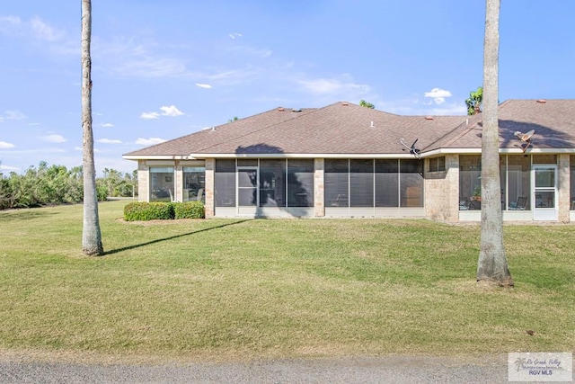 rear view of property featuring a yard, brick siding, roof with shingles, and a sunroom