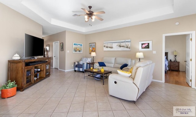 living room featuring light tile patterned floors, ceiling fan, a raised ceiling, and baseboards