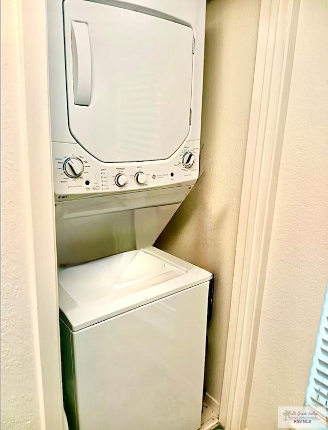 laundry area featuring laundry area, a textured wall, and stacked washer and clothes dryer