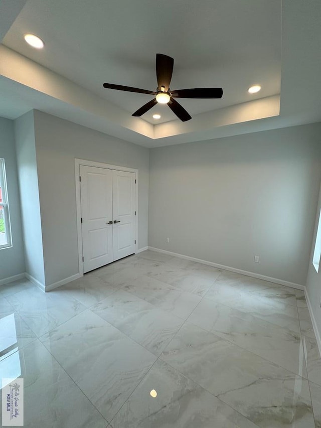 unfurnished bedroom with a raised ceiling, ceiling fan, and a closet