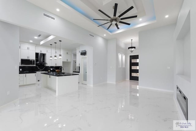 kitchen featuring exhaust hood, ceiling fan with notable chandelier, hanging light fixtures, a kitchen island, and white cabinetry