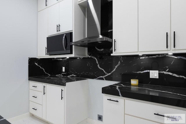 kitchen featuring decorative backsplash, white cabinetry, dark stone counters, and wall chimney range hood