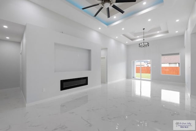 unfurnished living room featuring ceiling fan with notable chandelier and a raised ceiling