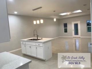 kitchen with pendant lighting, white cabinetry, sink, and a kitchen island with sink