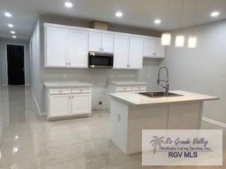 kitchen featuring decorative light fixtures, sink, white cabinetry, and a kitchen island with sink