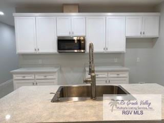 kitchen with white cabinets, light stone counters, and sink