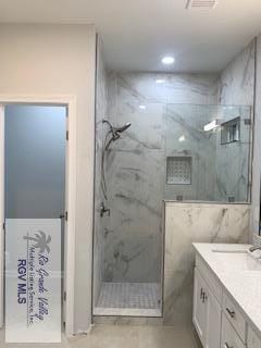 bathroom featuring vanity, a tile shower, and tile walls