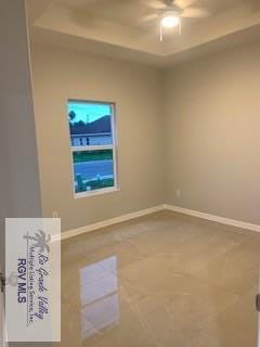 empty room featuring tile patterned flooring, ceiling fan, and a raised ceiling