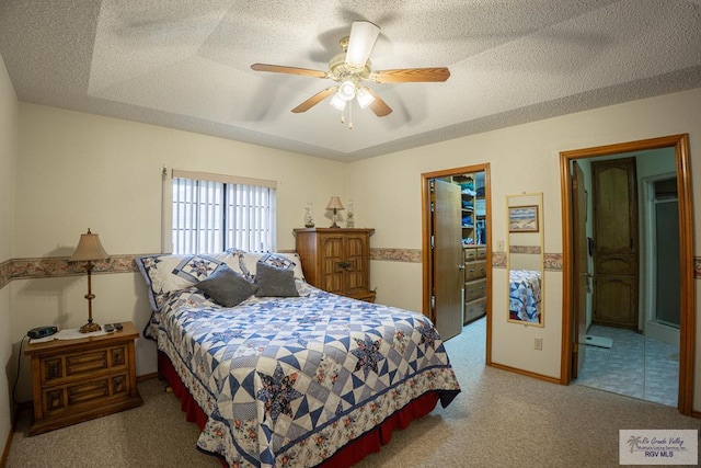 bedroom featuring a spacious closet, a textured ceiling, a raised ceiling, ceiling fan, and light colored carpet