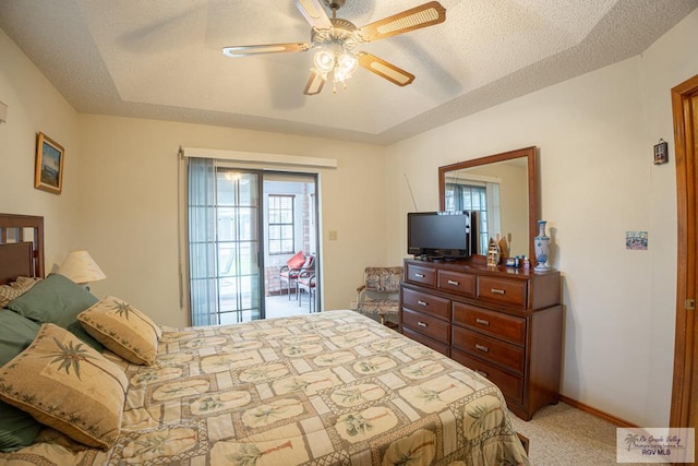 carpeted bedroom featuring a textured ceiling, ceiling fan, and a raised ceiling