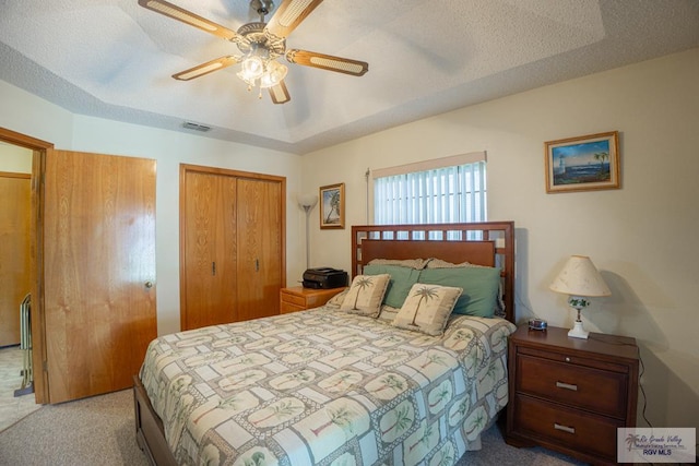 bedroom with light carpet, ceiling fan, multiple closets, a tray ceiling, and a textured ceiling