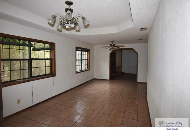 tiled empty room with baseboards, a tray ceiling, a textured ceiling, and visible vents