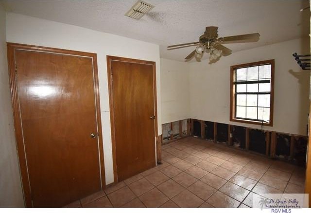 unfurnished bedroom featuring tile patterned flooring, a textured ceiling, two closets, a ceiling fan, and visible vents