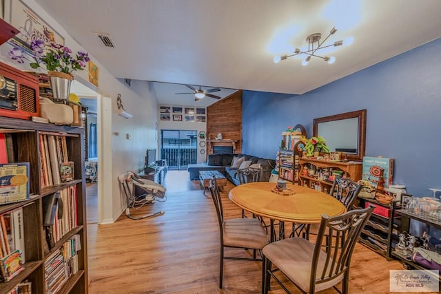 dining room featuring ceiling fan with notable chandelier, wood walls, light wood-type flooring, and vaulted ceiling