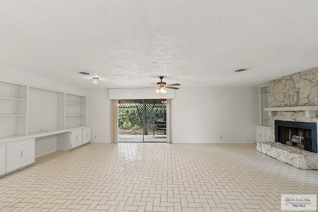 unfurnished living room with ceiling fan, a stone fireplace, built in features, and a textured ceiling