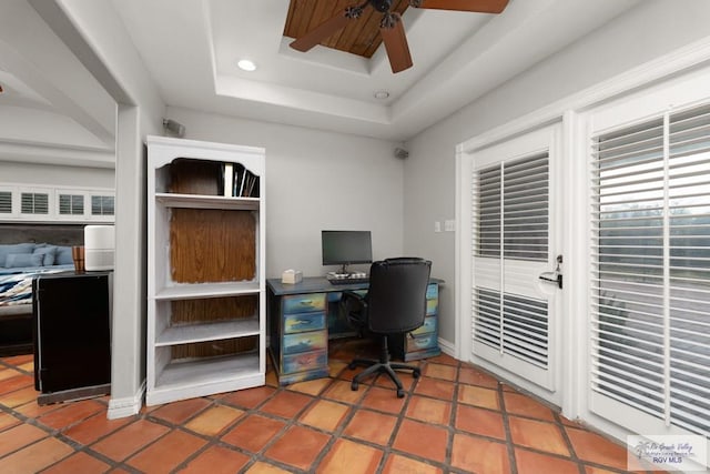 office space with tile patterned floors, ceiling fan, and a tray ceiling