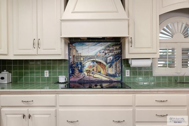 kitchen with premium range hood, tile countertops, backsplash, and white cabinets