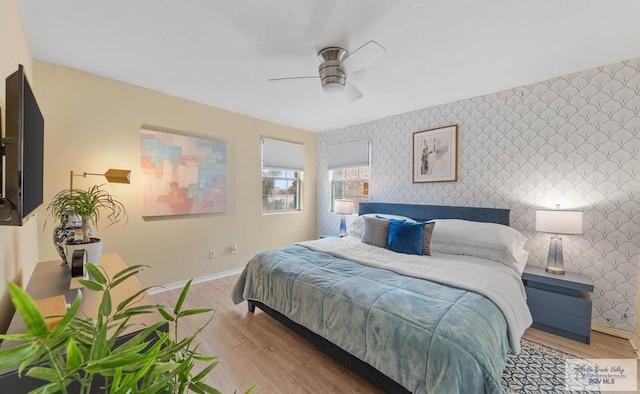 bedroom with wallpapered walls, an accent wall, baseboards, and wood finished floors