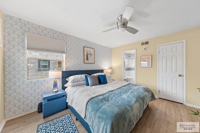 bedroom featuring an accent wall, wood finished floors, visible vents, baseboards, and wallpapered walls