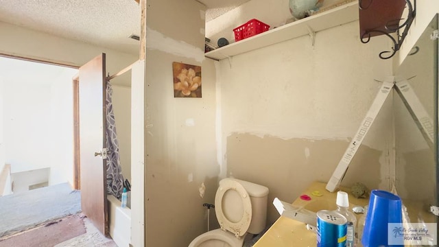 bathroom featuring a textured ceiling, toilet, and shower / bath combo with shower curtain